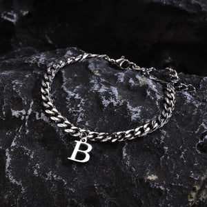 Silver Cuban link initial bracelet with the letter B lying on dark stone