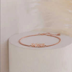 Rose gold capital letter name bracelet with the name ROSIE on a round stand