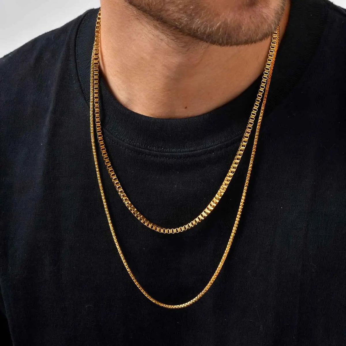 Two gold box chain necklaces layered over a black T-shirt