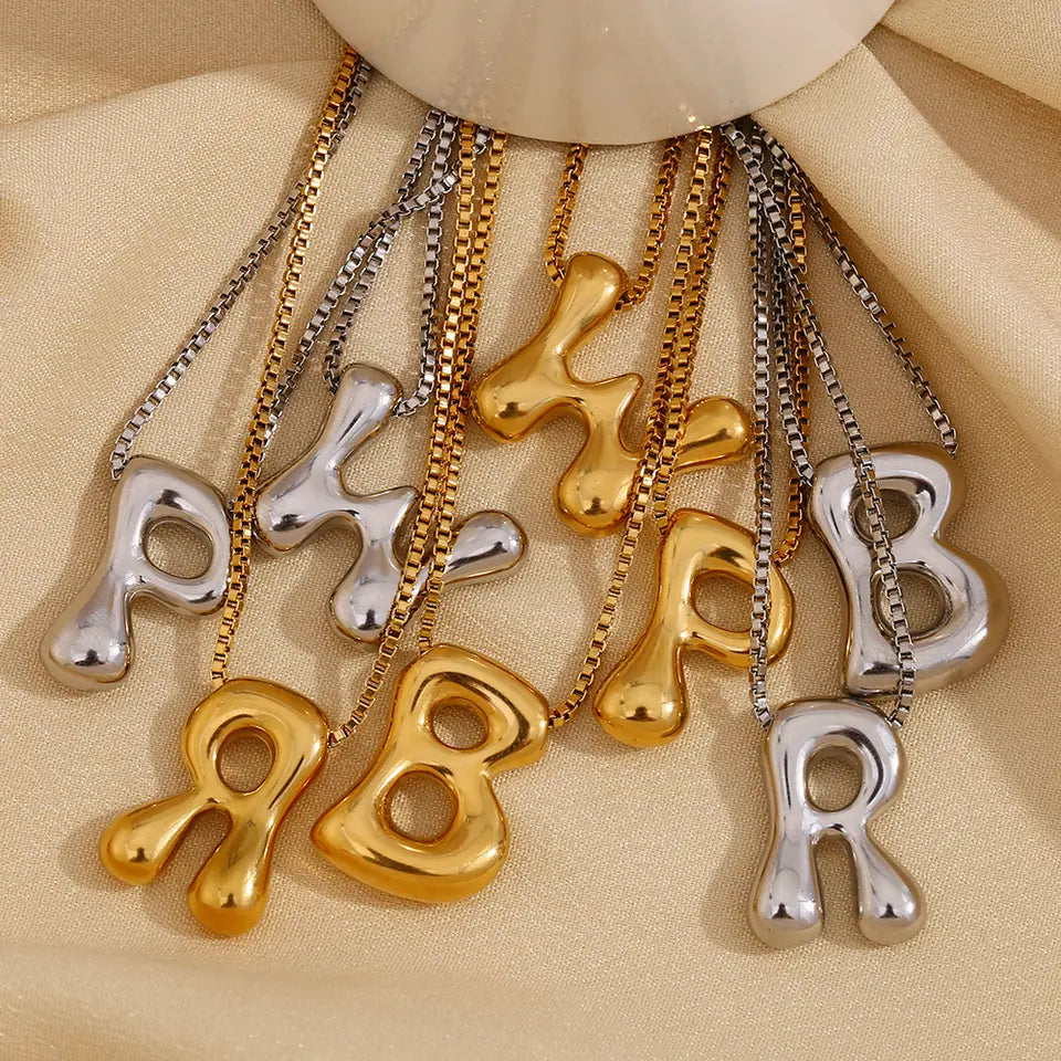 Bold Bubble Initial Pendant Necklace gold and silver letter variants on beige fabric