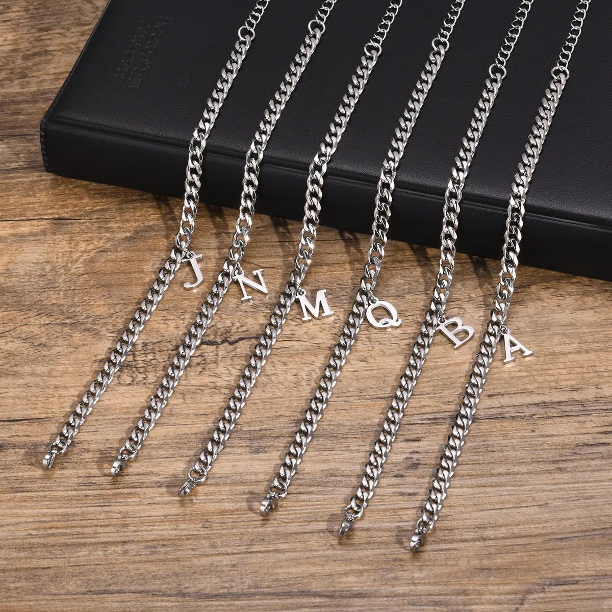 Six silver Cuban link initial bracelets with letters J, N, M, Q, B and A lying flat