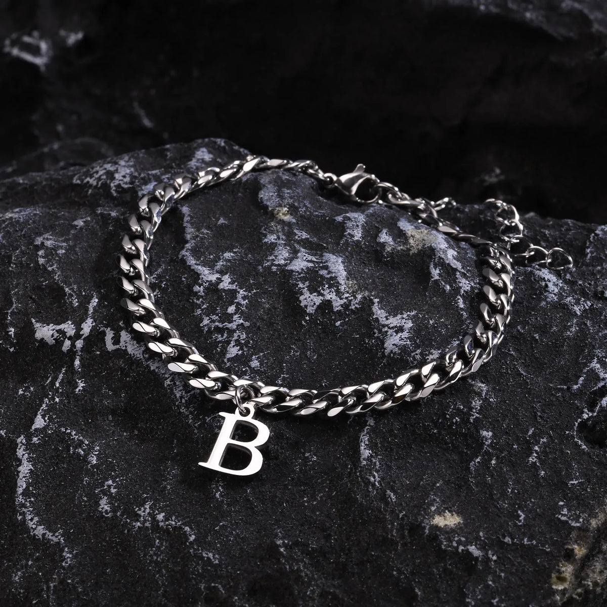 Silver Cuban link initial bracelet with the letter B lying on dark stone
