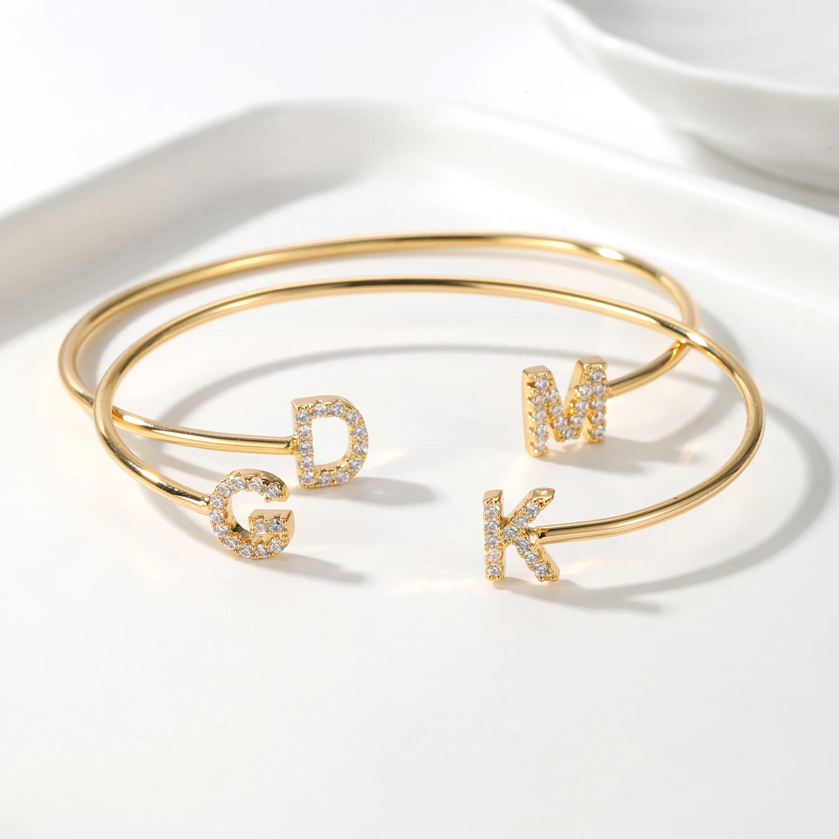 Two gold double initial cuff bracelets with the letters G, D, M and K