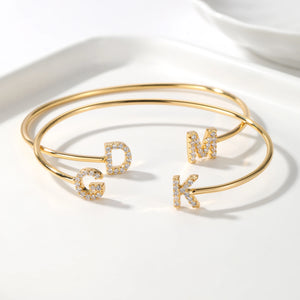 Two gold double initial cuff bracelets with the letters G, D, M and K