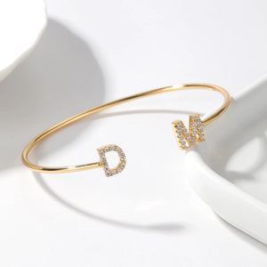 Gold double initial cuff bracelet with the letters D and M on a white surface