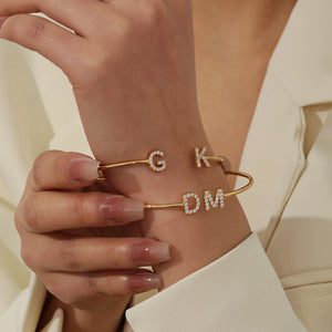 Two gold double initial cuff bracelets with G, K and D, M worn on the wrist