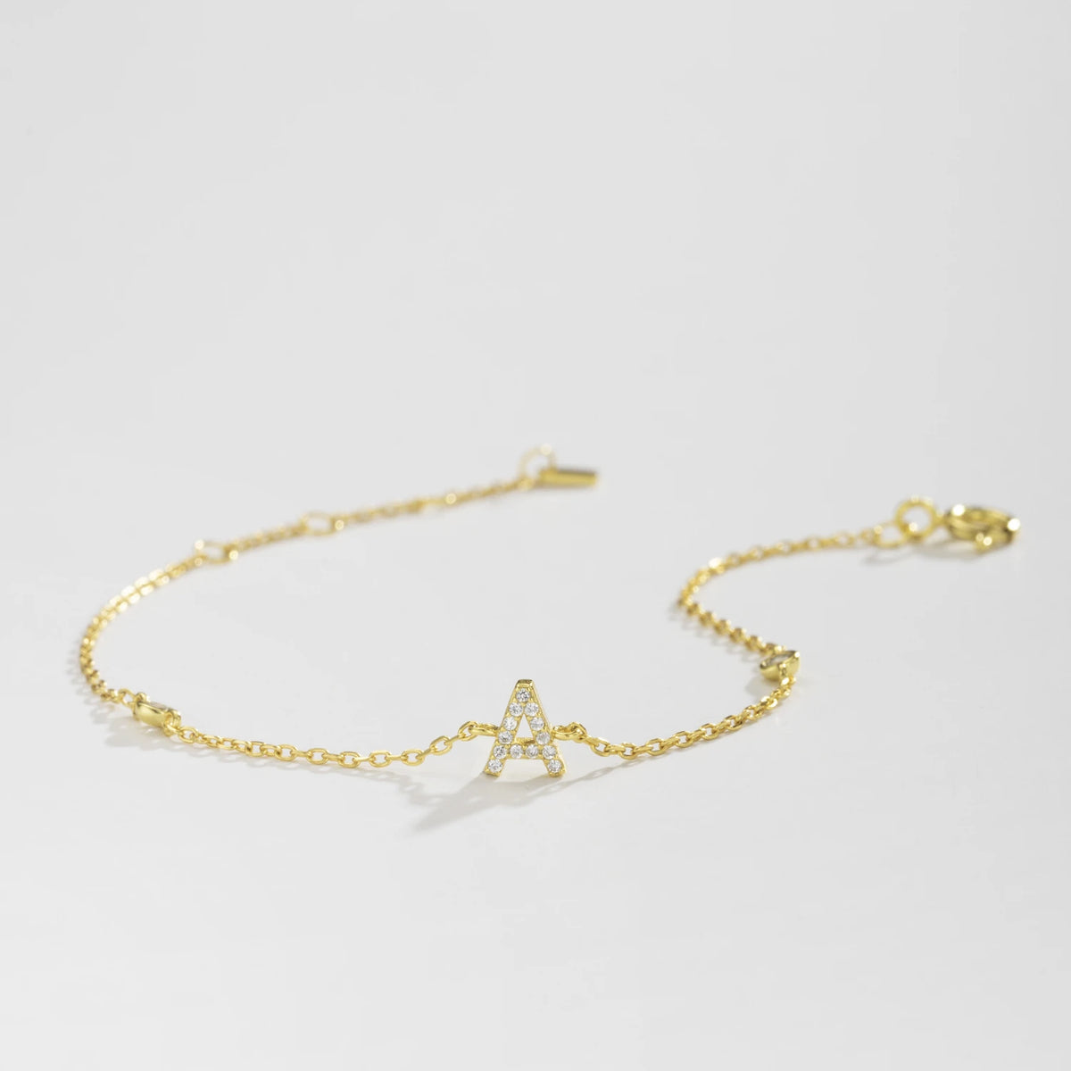 Gold dainty initial bracelet with the letter A lying on a white surface