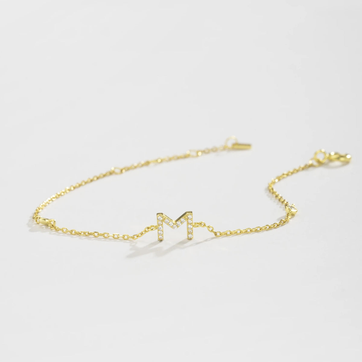 Gold dainty initial bracelet with the letter M lying on a white surface