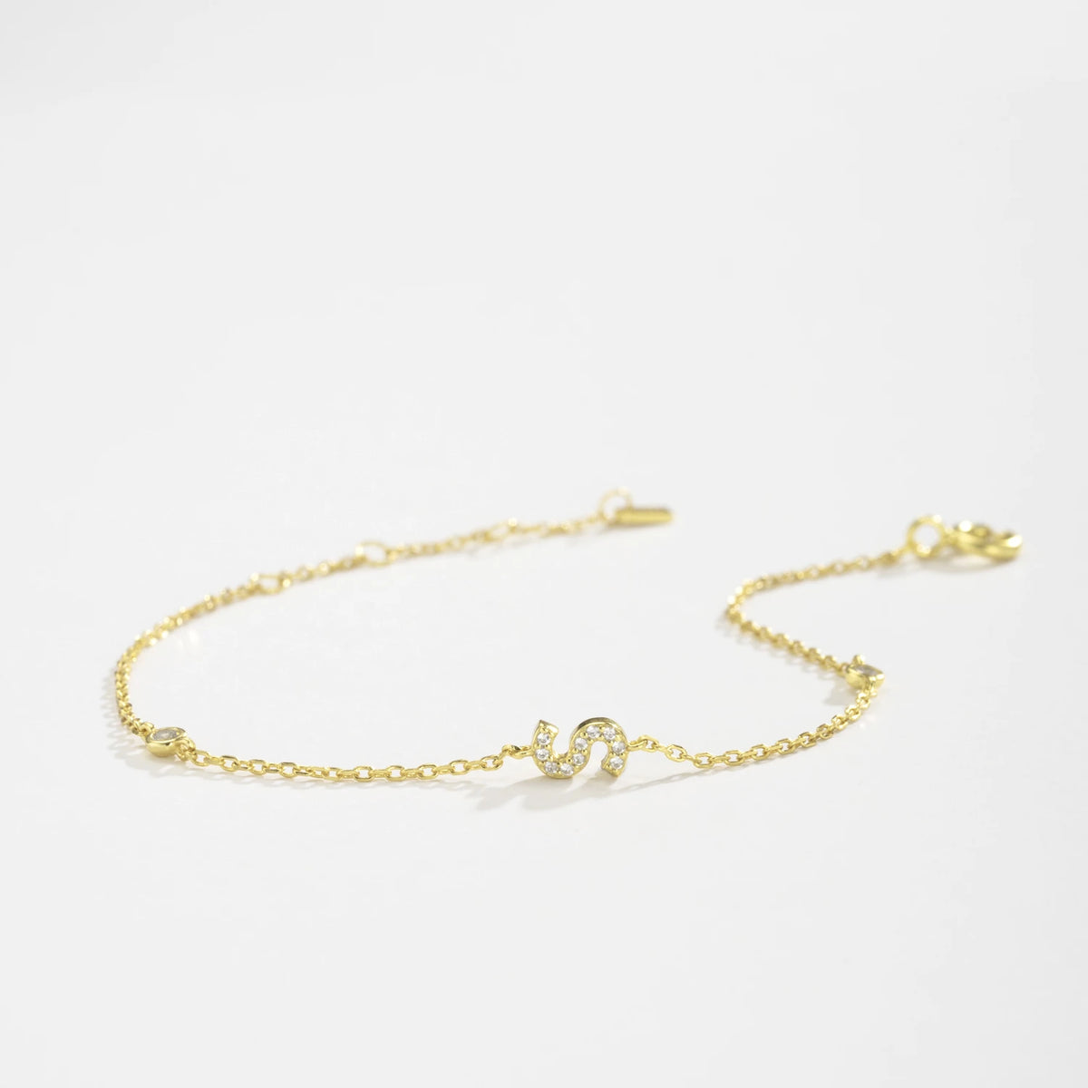 Gold dainty initial bracelet with the letter S lying on a white surface