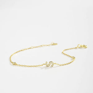 Gold dainty initial bracelet with the letter S lying on a white surface