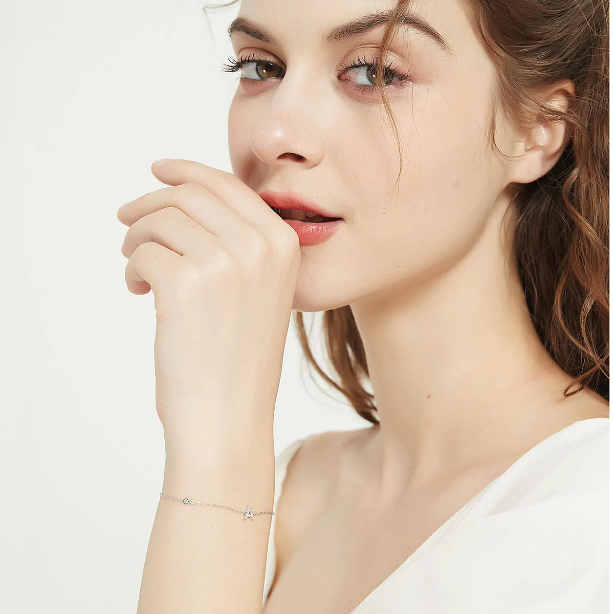 Dainty initial bracelet worn on the wrist, hand raised to the face