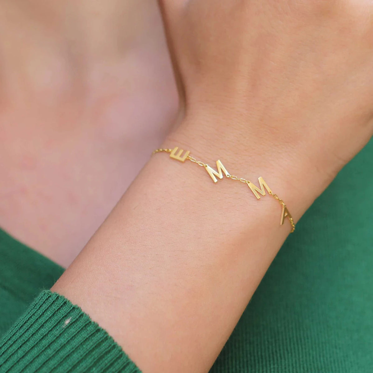 Gold multiple initials bracelet with the letters EMMA worn on the wrist
