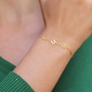 Gold multiple initials bracelet with the letters EMMA worn on the wrist