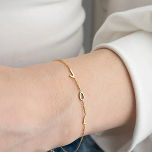 Gold multiple initials bracelet with three letters worn on the wrist