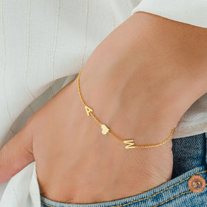 Close-up of a gold initials bracelet A and M with a heart on the wrist