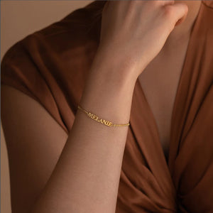 Gold capital letter name bracelet with the name MELANIE worn on the wrist