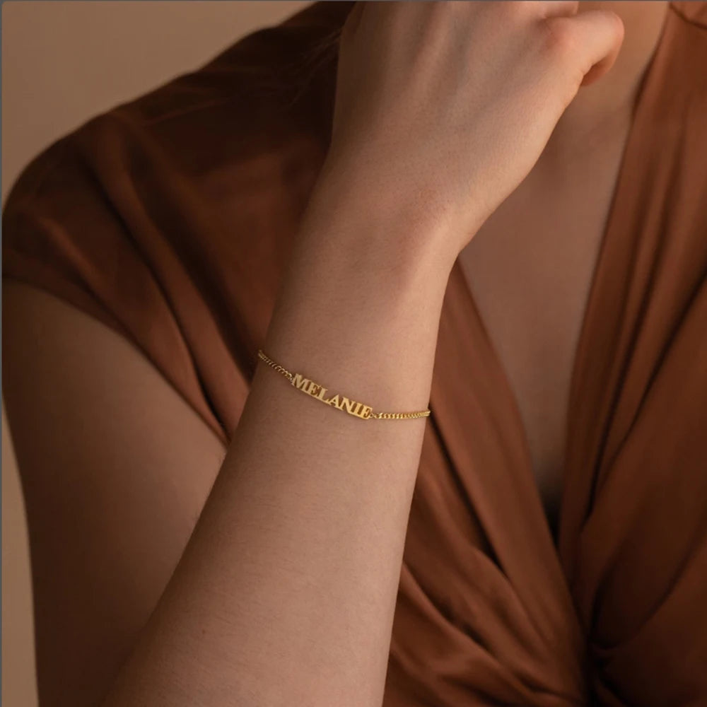 Gold capital letter name bracelet with the name MELANIE worn on the wrist