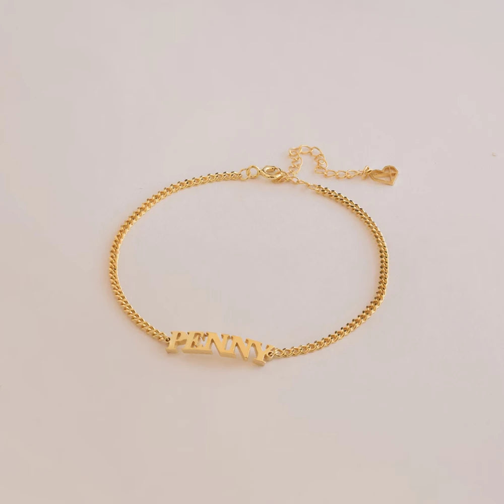Gold capital letter name bracelet with the name PENNY lying flat