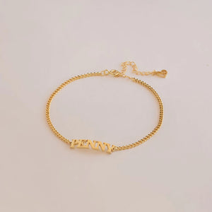 Gold capital letter name bracelet with the name PENNY lying flat