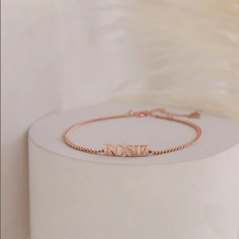 Rose gold capital letter name bracelet with the name ROSIE on a round stand