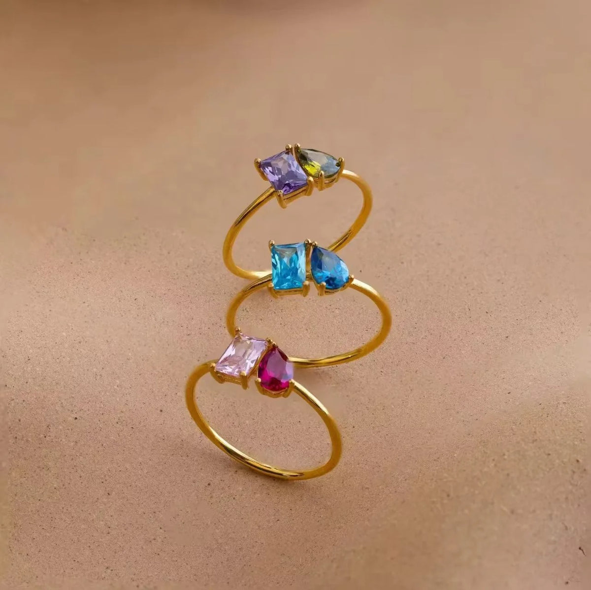 Three gold double birthstone rings with purple, blue and pink stones